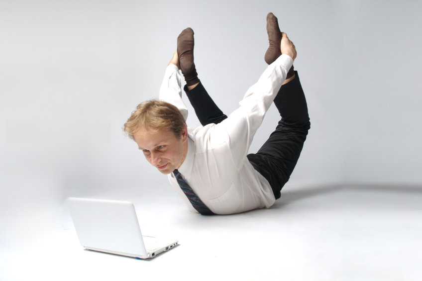 Junger Mann im Anzug macht vor geöffnetem Laptop Yoga